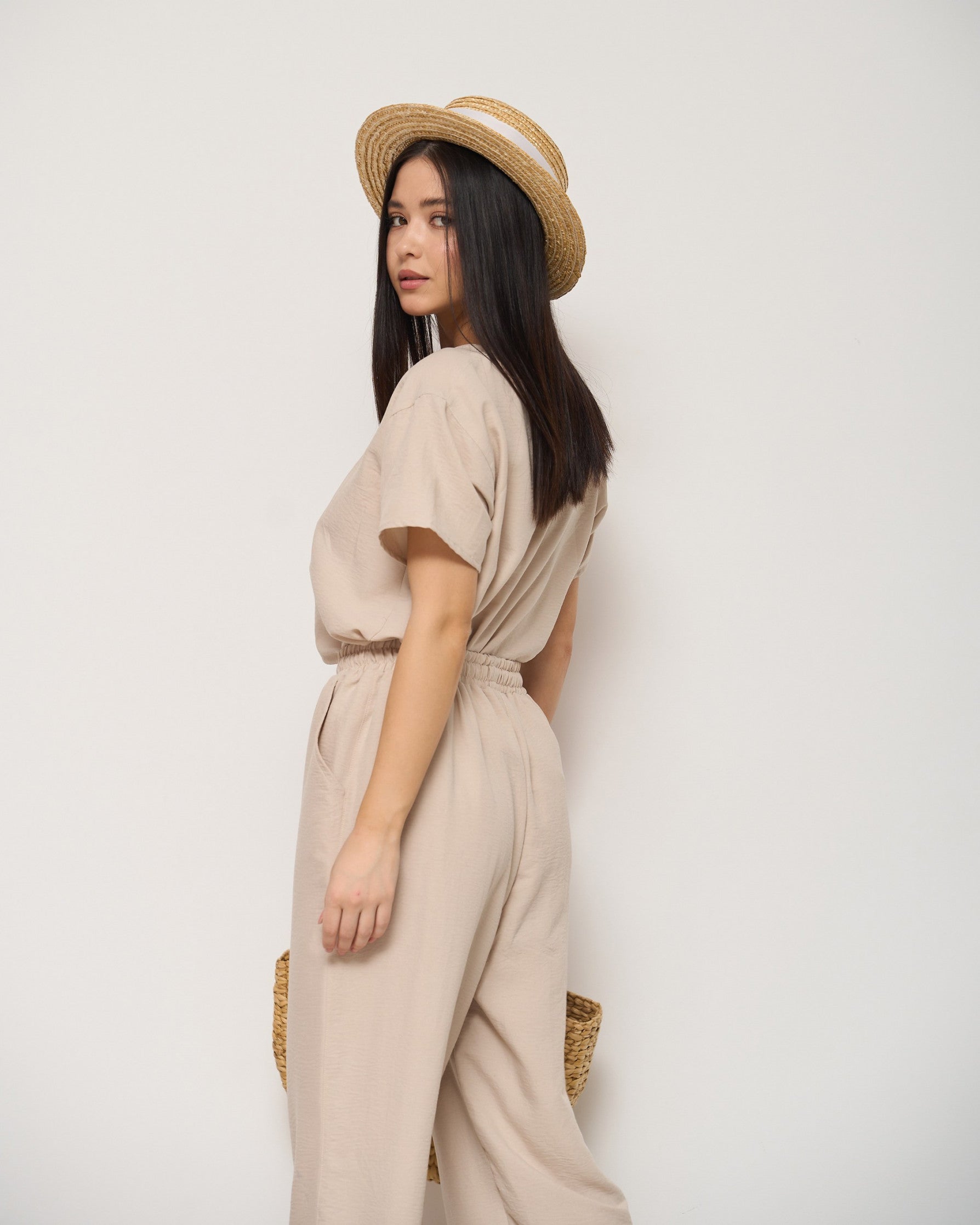 Back view of a model wearing a beige pyjama set with a drawstring waist and a straw hat, showcasing the relaxed and comfortable fit by Popjammies.