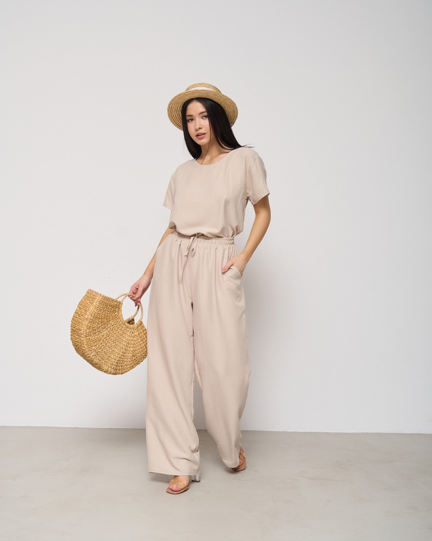 Model wearing a beige pyjama set with a straw hat and woven bag, showcasing comfortable and stylish loungewear by Popjammies.