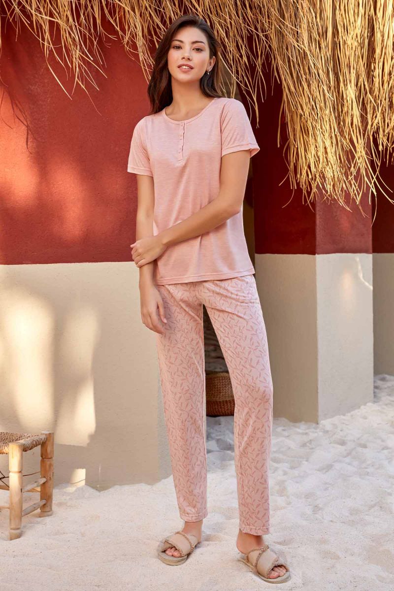 Model wearing Popjammies 'Sunset Bliss' Pyjama Set, featuring a peach-colored top with button detail and matching printed pants, standing in a warm, tropical outdoor setting.