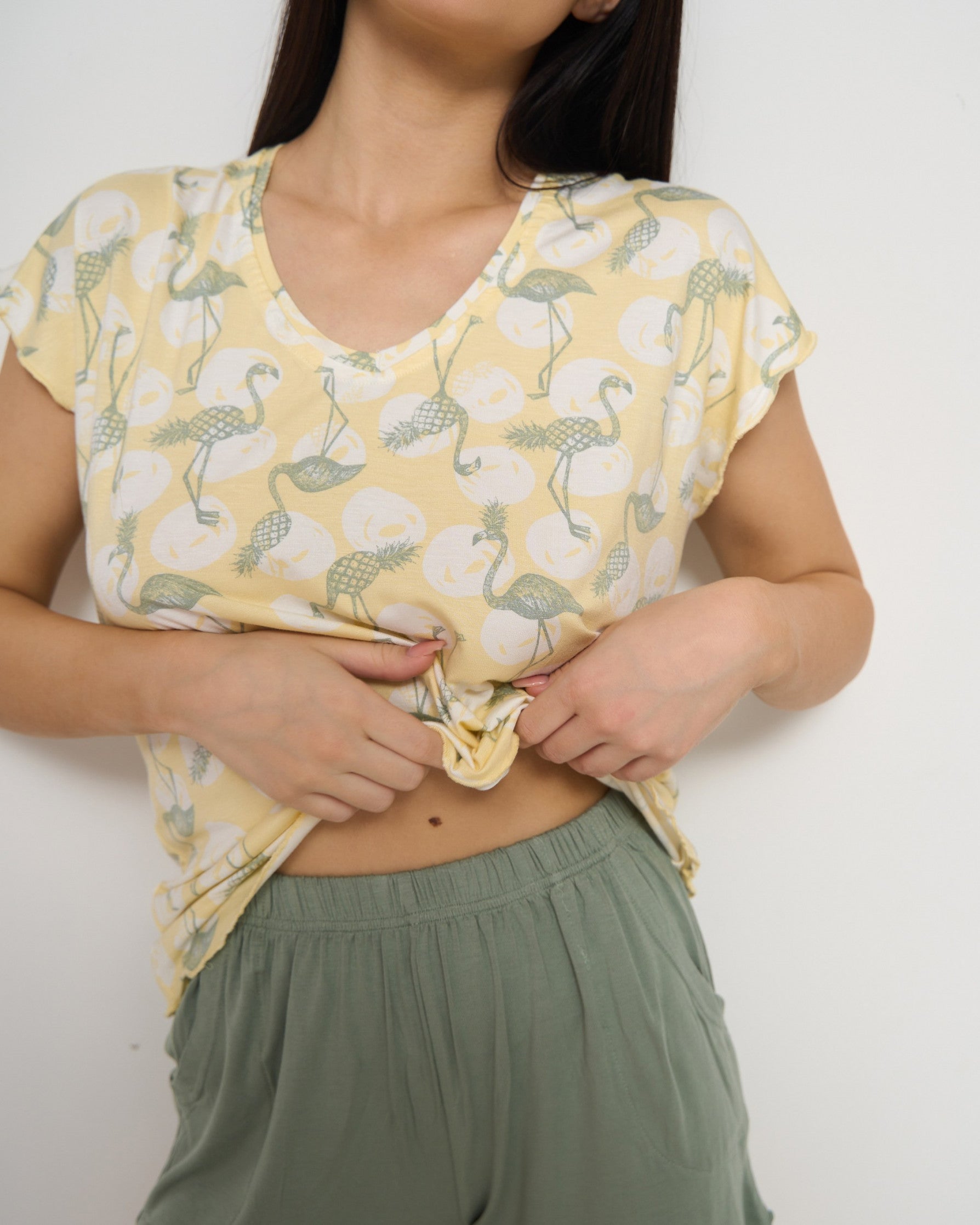 Close-up of a woman wearing a yellow flamingo print top and green shorts from Popjammies.