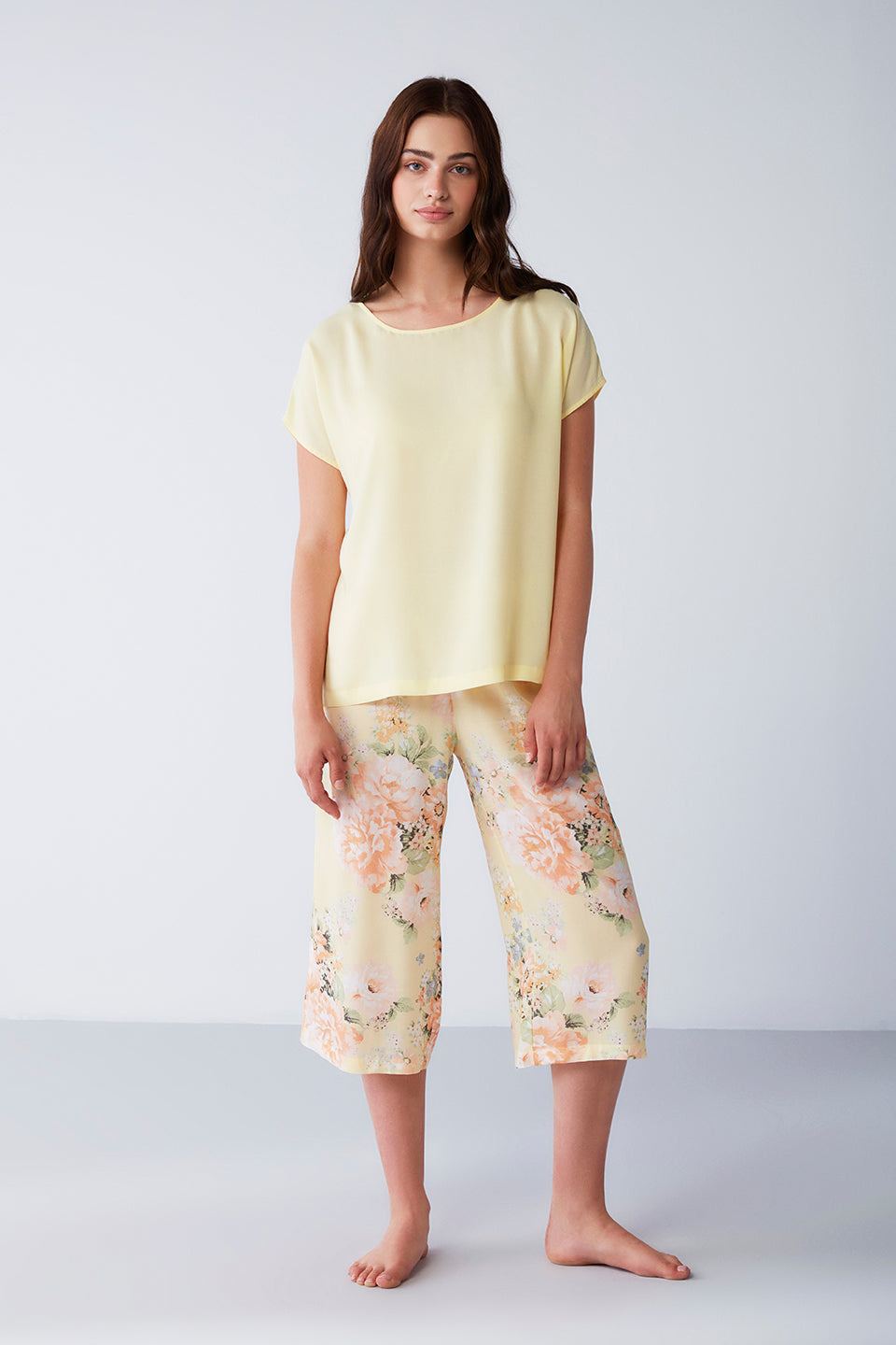 Woman wearing a yellow short-sleeve top with a round neckline and pastel floral patterned capri pants from the Popjammies Women's Yellow Short Sleeve Top with Floral Capri Pyjama Set.