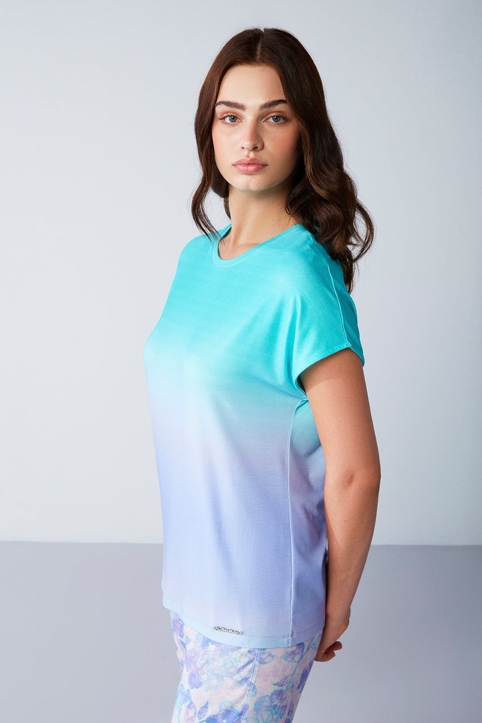 Model in a side profile view wearing a Popjammies Women's Pyjama Set with a gradient aqua to lavender top and floral print pants, against a plain background.