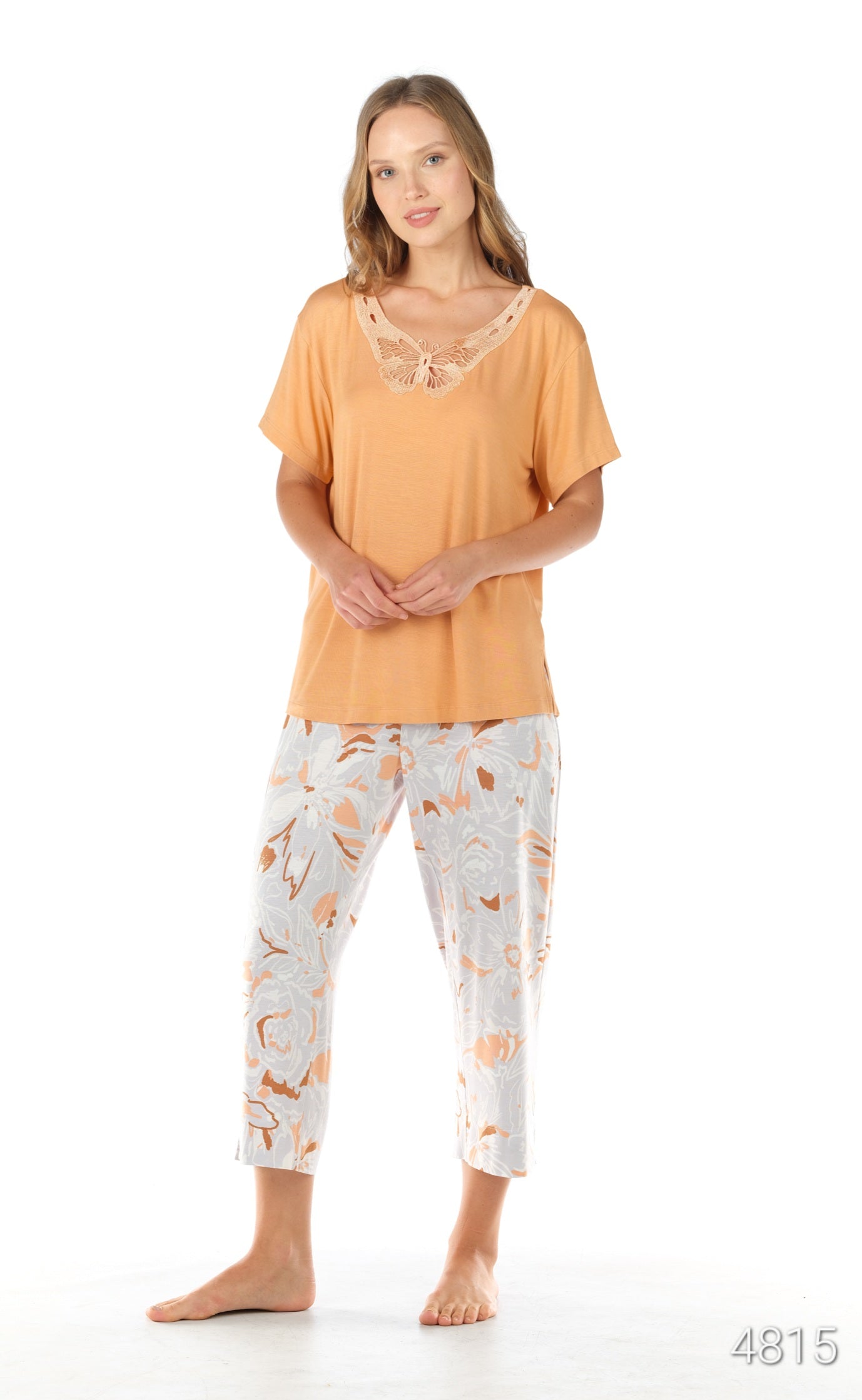 Woman wearing a peach short-sleeved top with a butterfly lace neckline and white floral patterned pants from the Popjammies Women's Butterfly Lace Pyjama Set.