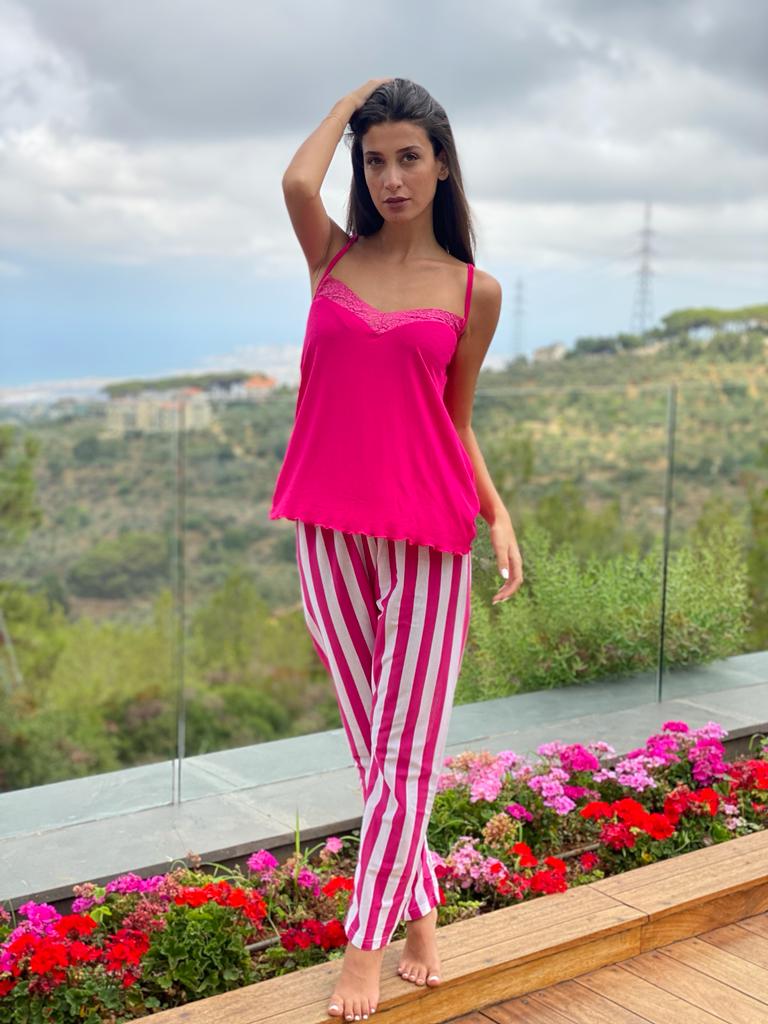 Woman in a pink camisole with lace trim and pink and white striped pants, posing in a garden.