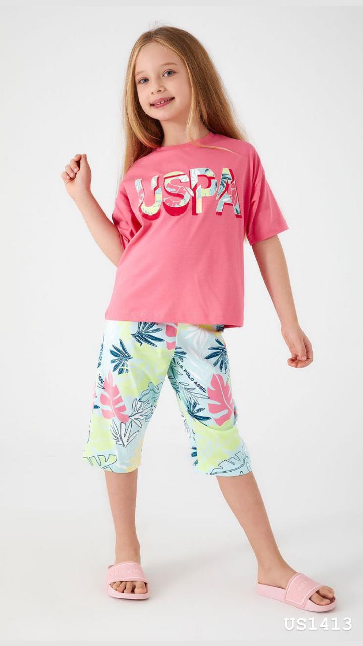 Smiling girl wearing a vibrant pink pyjama top with 'USPA' logo and tropical-print shorts, posing confidently.