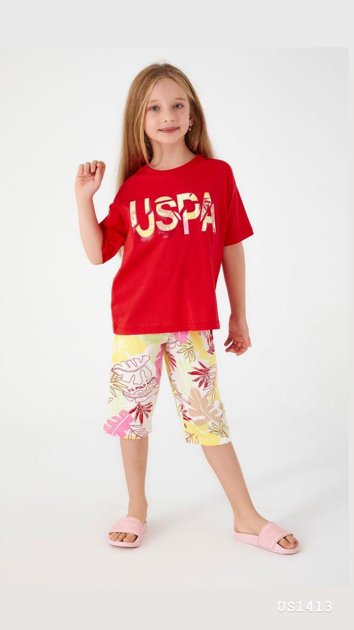 Smiling girl wearing a bright red pyjama top with 'USPA' logo and tropical-print shorts, posing confidently.