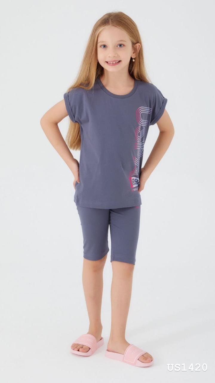 Child wearing the Popjammies Midnight Charm Pajama Set, featuring a dark gray T-shirt with a vertical "Pop" graphic in pastel colors and matching shorts, smiling and looking comfortable.