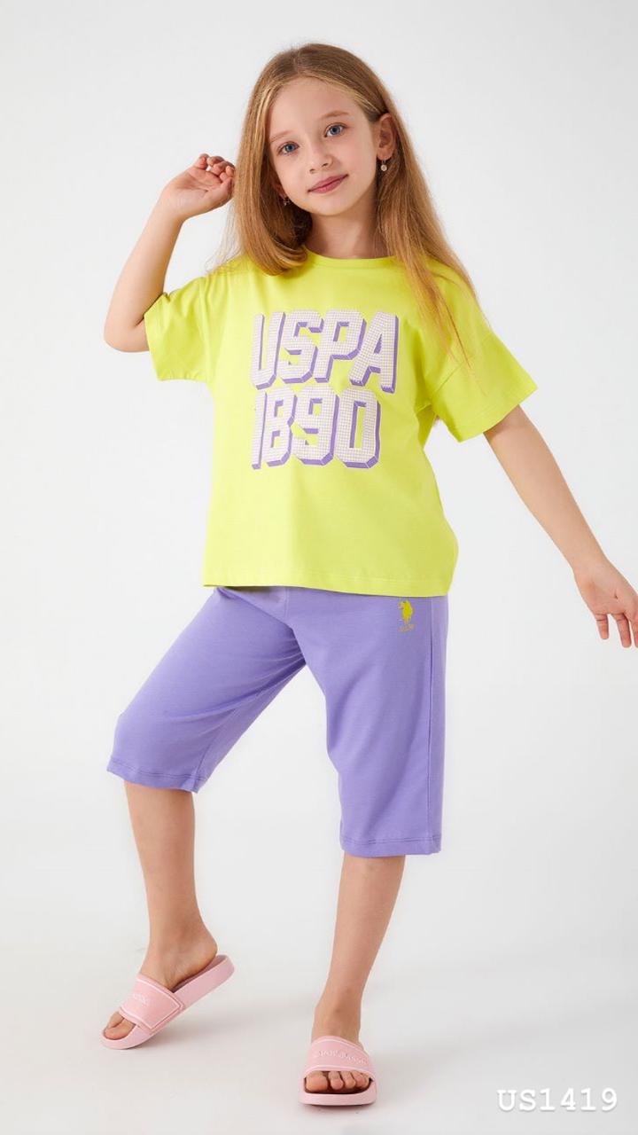 Smiling girl wearing a bright yellow and purple pyjama set with 'USPA 1890' print, posing confidently.