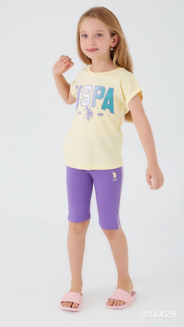 Child wearing the Popjammies Sunshine & Lavender Pajama Set, featuring a yellow T-shirt with a "USPA" graphic print and lavender capri pants, smiling and looking comfortable.