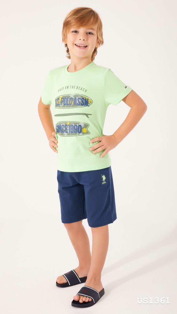 Boy standing with hands on hips, wearing a light green top with "POLO ON THE BEACH" and "US POLO ASSN SINCE 1890" graphics, and navy blue shorts from Popjammies.