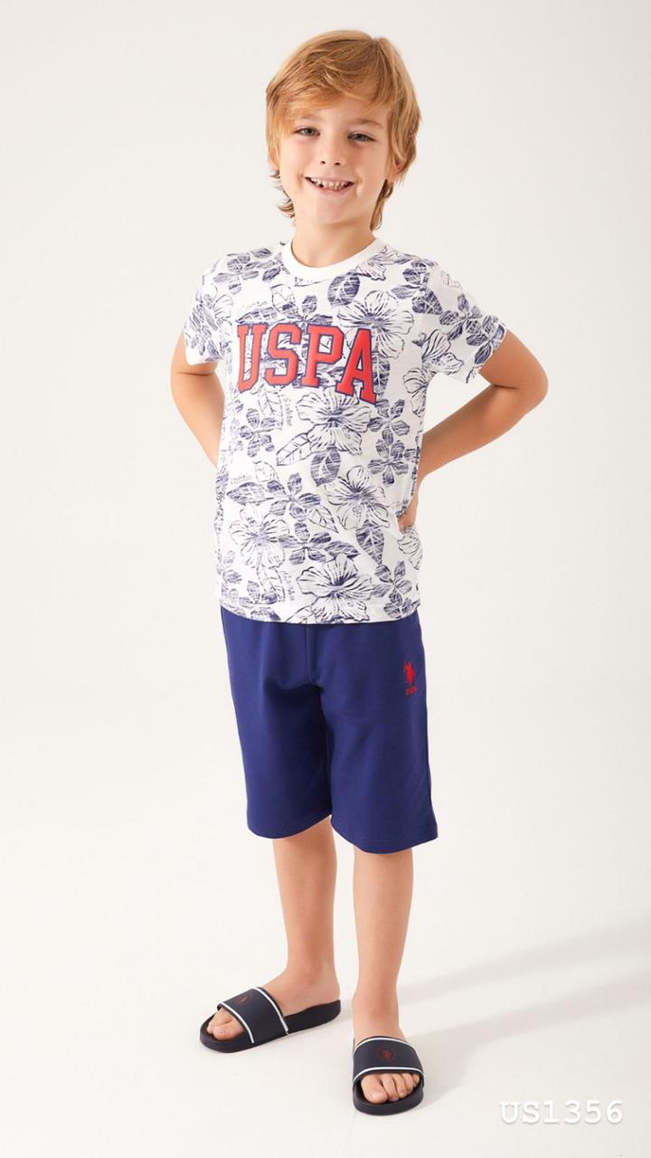 Boy standing in Popjammies pajama set with a white floral print top and blue shorts, hands on hips, smiling.