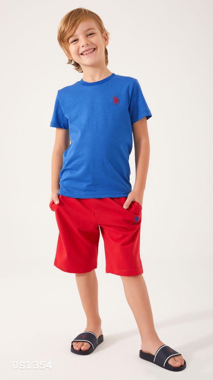  A young boy wearing a vibrant blue top with a red USPA logo and matching red shorts, smiling with hands in pockets.