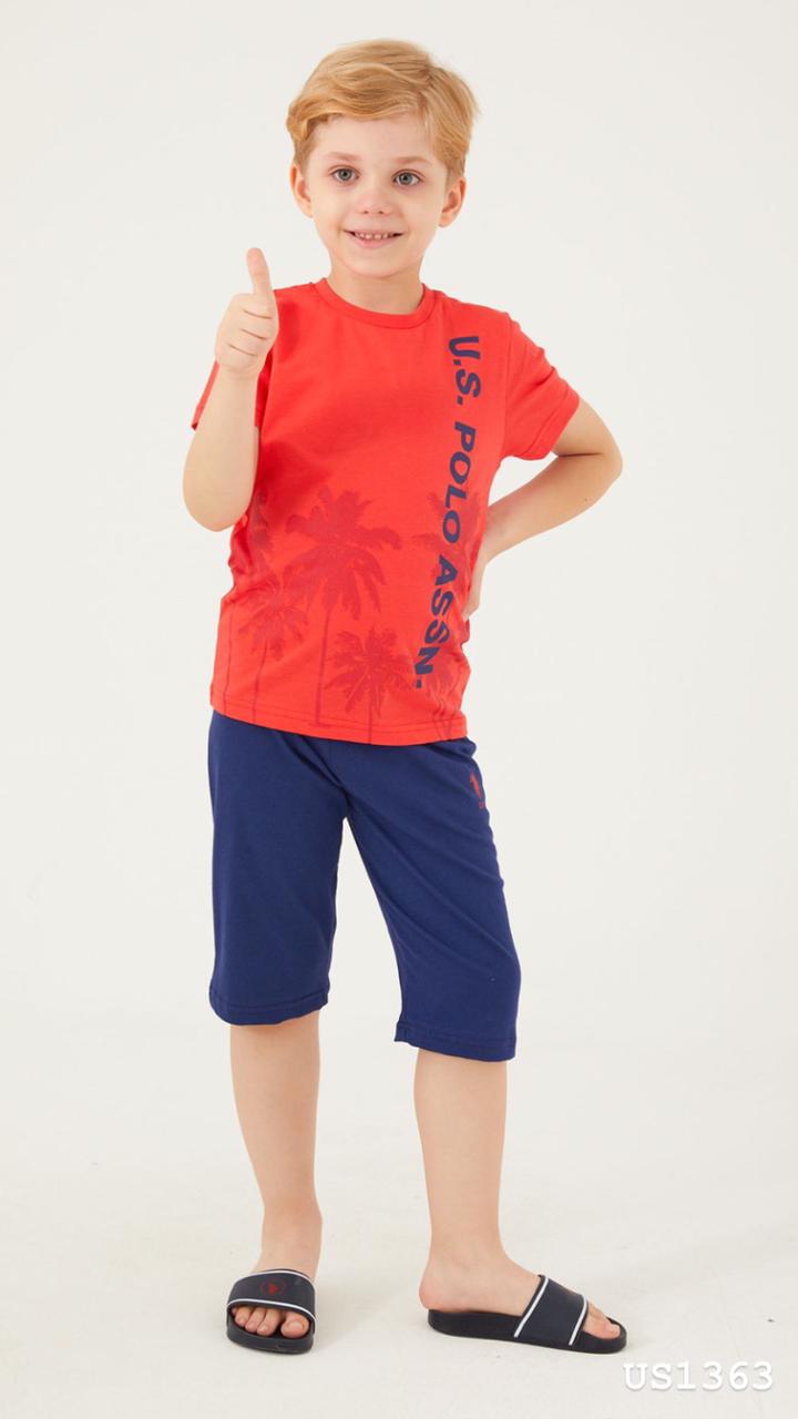 Smiling boy wearing a red top with "U.S. POLO ASSN." logo and palm tree graphic, paired with navy blue shorts pyjama set from Popjammies, giving a thumbs up.