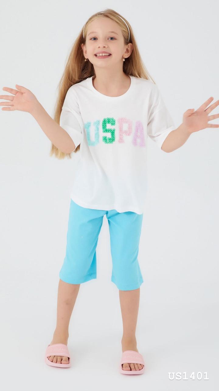 Smiling girl wearing a colorful pyjama set with a white top featuring a multi-colored "USPA" logo and bright blue capri pants from Popjammies.