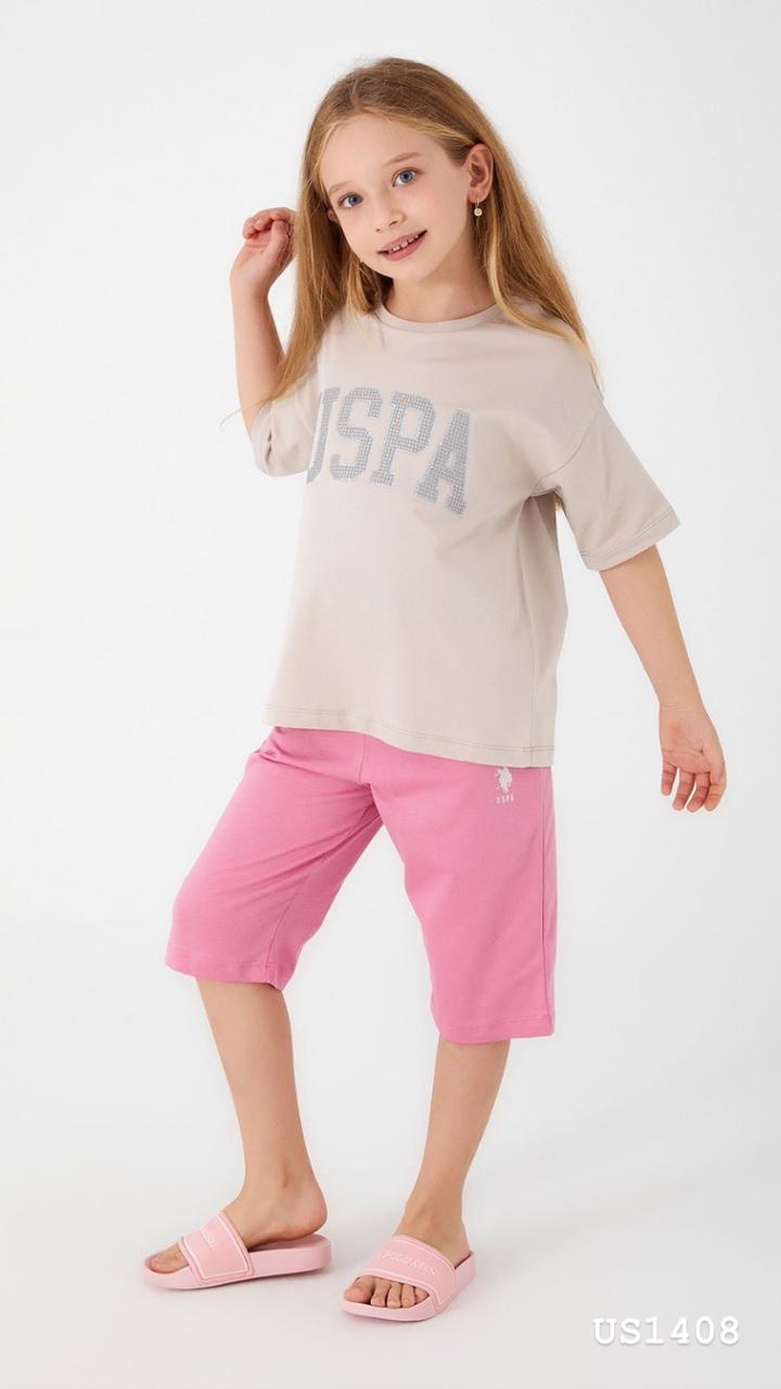 Smiling girl wearing a beige pyjama top with a sparkling 'USPA' logo and pink shorts from Popjammies.