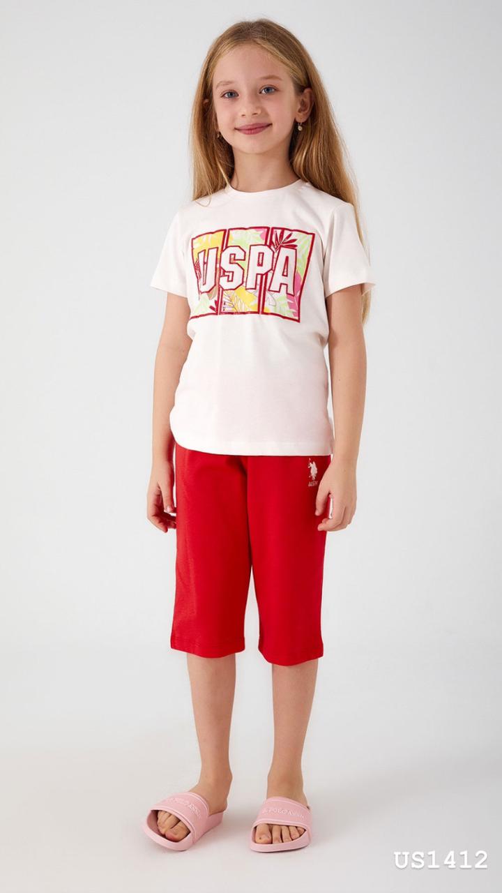 Smiling girl wearing a white pyjama top with 'USPA' logo and tropical motif, paired with bold red shorts.