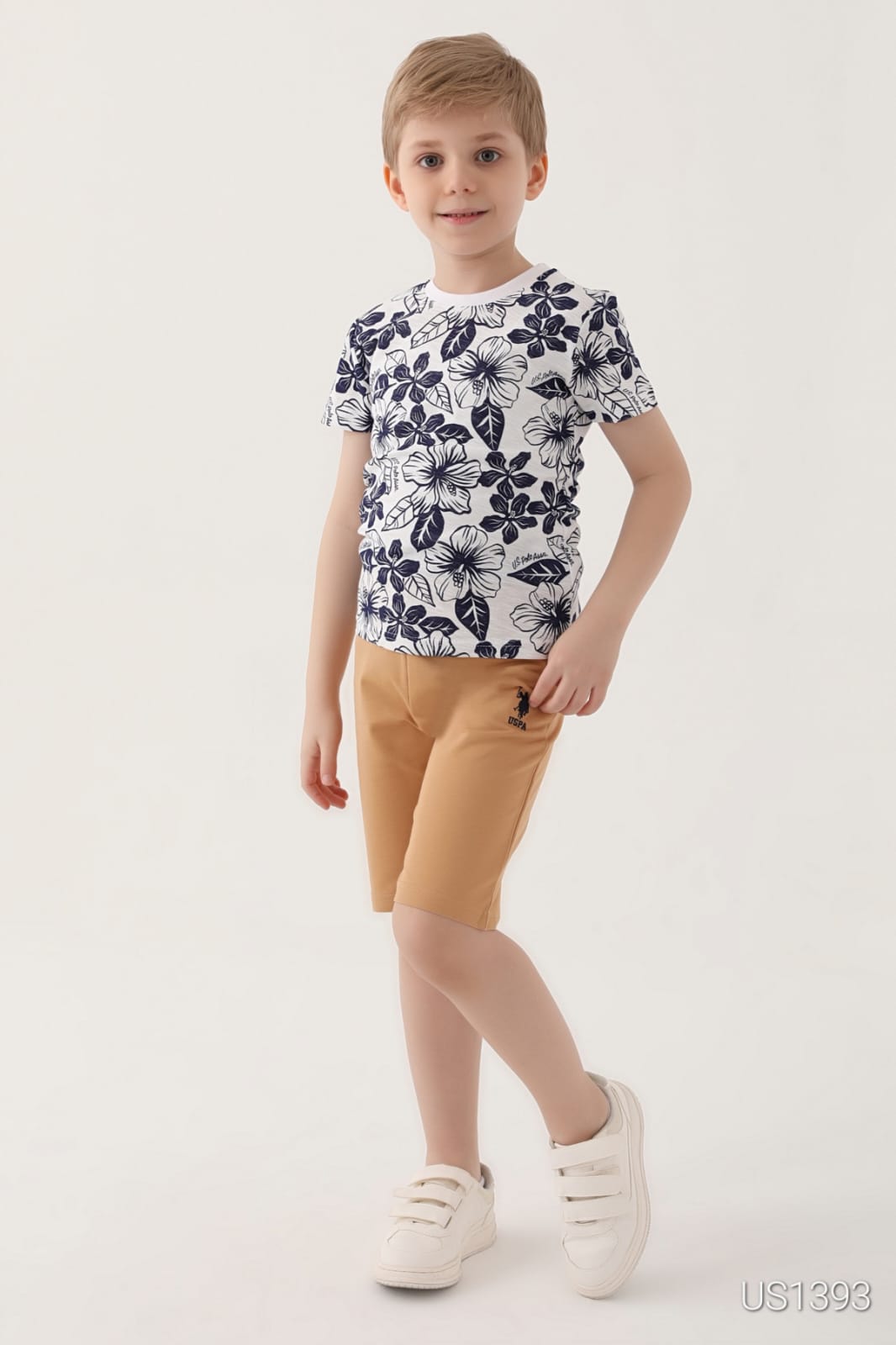 Smiling boy wearing a navy blue floral print top and light brown shorts pyjama set from Popjammies.