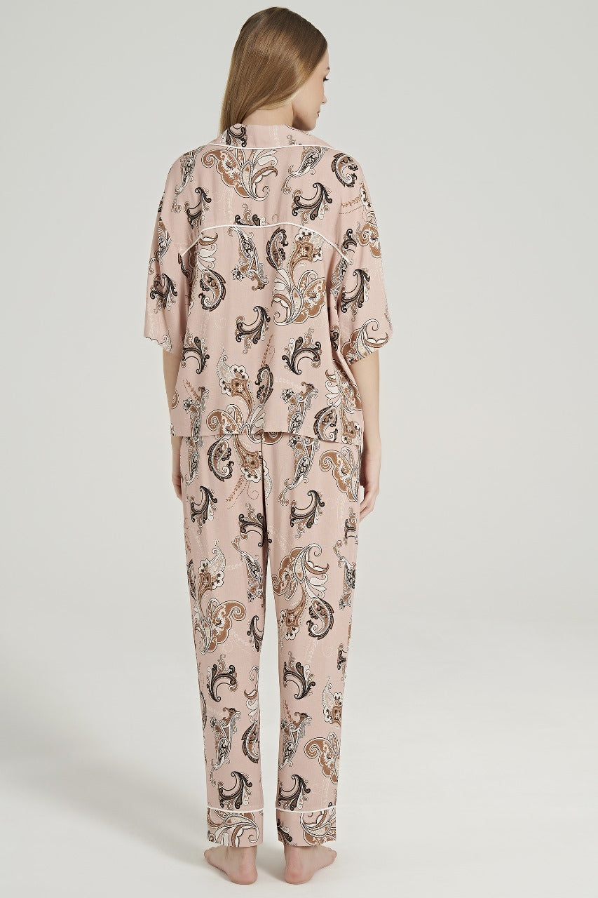 Rear view of a model wearing the Popjammies Women's Paisley Print Pyjama Set, featuring a soft, button-up top with a notched collar and short sleeves, and matching relaxed-fit pants adorned with an intricate paisley pattern in warm, earthy tones.