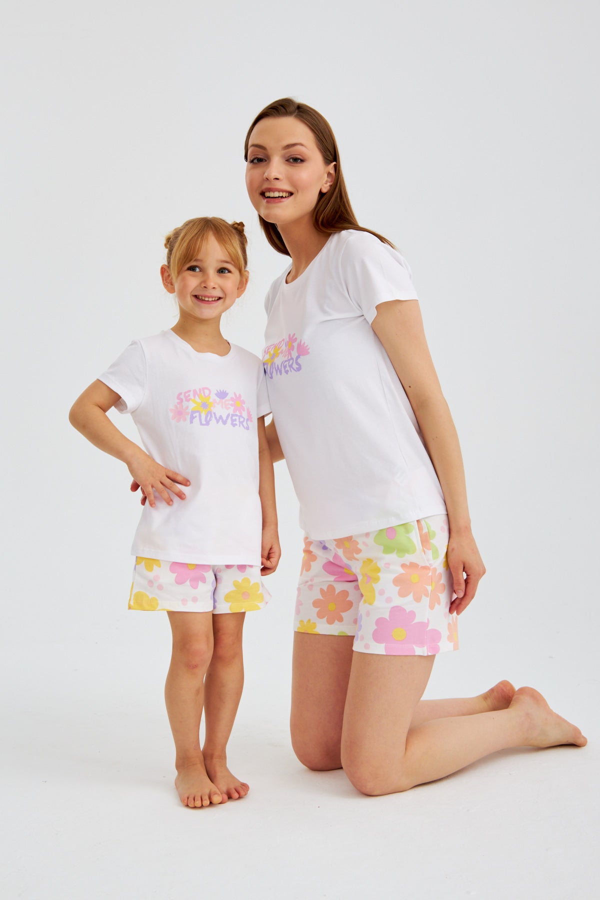 Mother kneeling next to daughter, both wearing the Popjammies "Send Me Flowers" pajama set, smiling and looking at the camera.