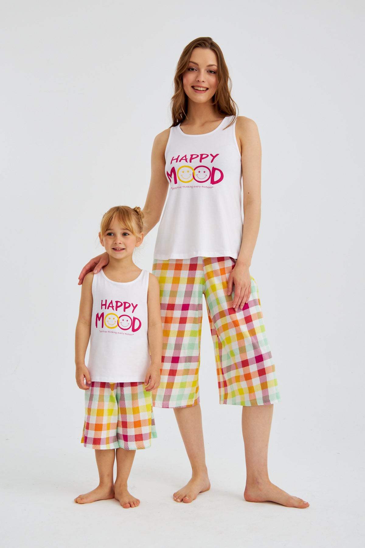 Mother and daughter wearing matching "Happy Mood" pyjama sets from Popjammies, standing and smiling.