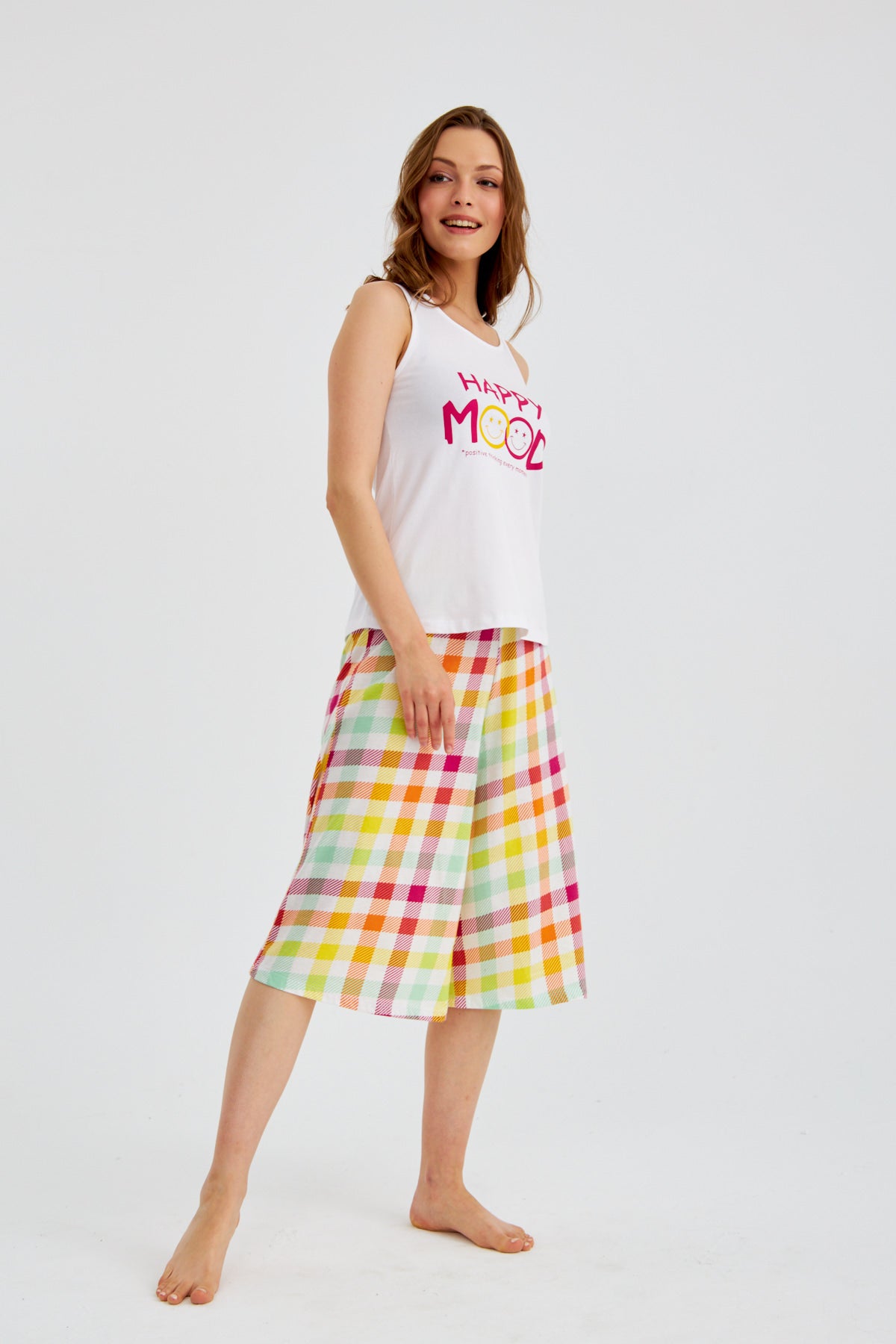 Woman wearing Happy Mood Checkered Pajama Set by Popjammies, featuring a white sleeveless top with "Happy Mood" graphic and colorful checkered pantacour.