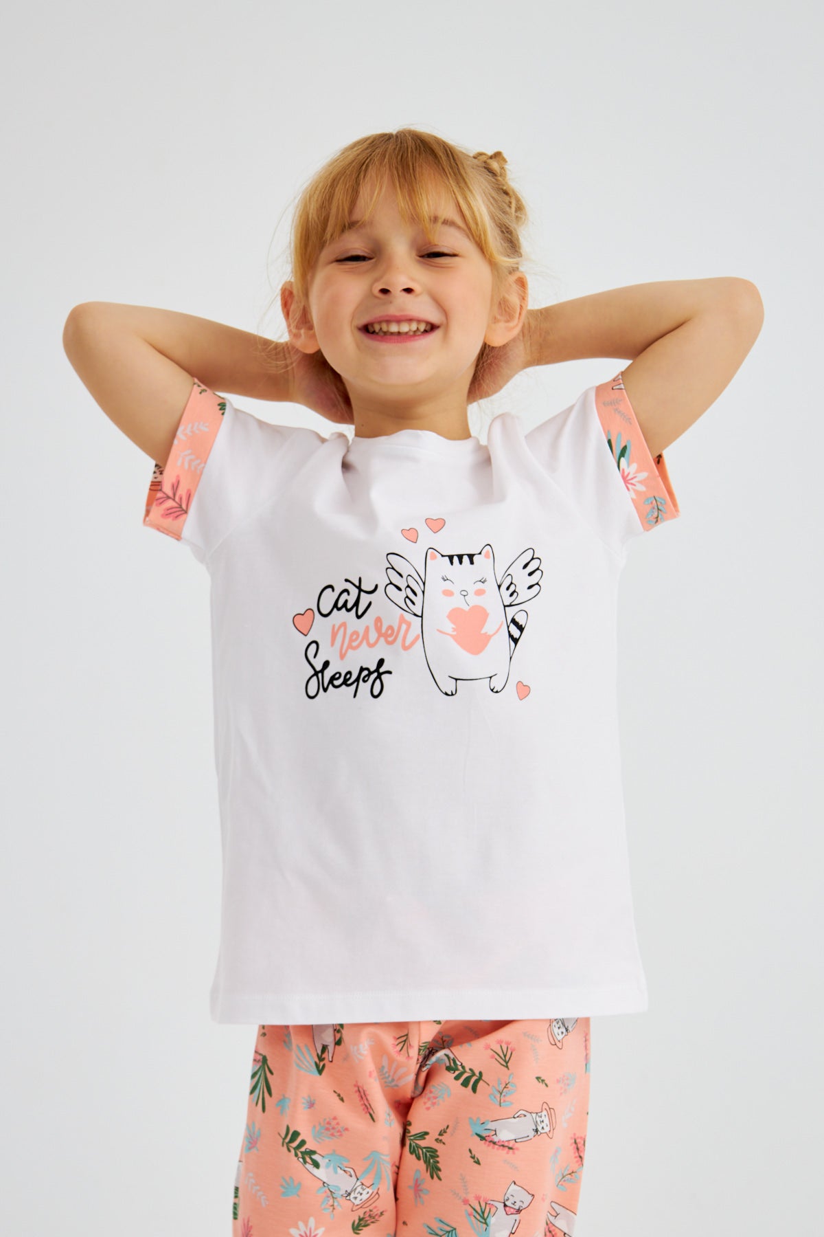 Close-up of a young girl smiling and wearing Popjammies "Cat Never Sleeps" pyjama set, featuring a white top with cat graphic and pink floral print pants.