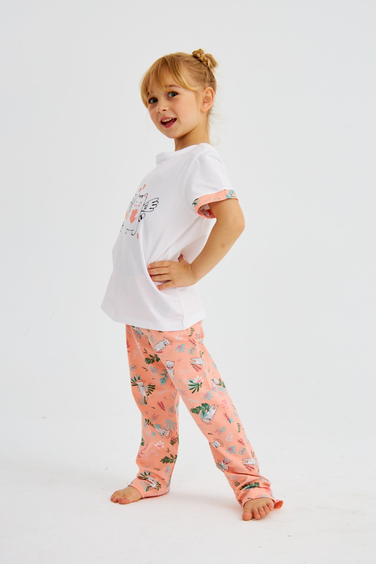 Young girl posing in Popjammies "Cat Never Sleeps" pyjama set, with white top featuring a cat graphic and pink floral print pants, smiling.