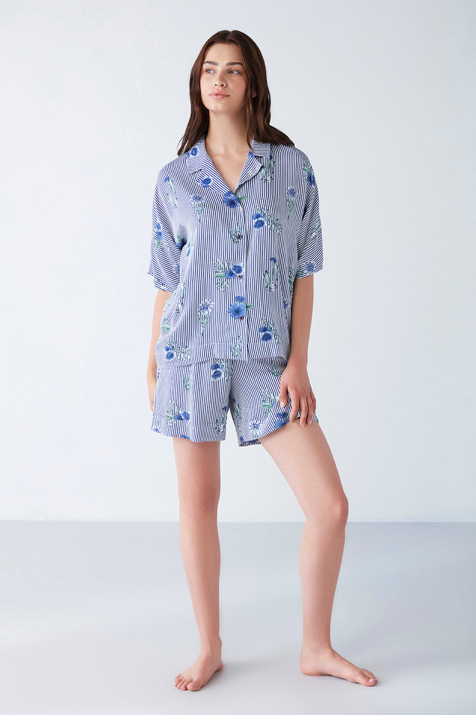 Woman wearing a blue striped floral print pyjama set from Popjammies, featuring a collared button-up top with short sleeves and matching shorts.