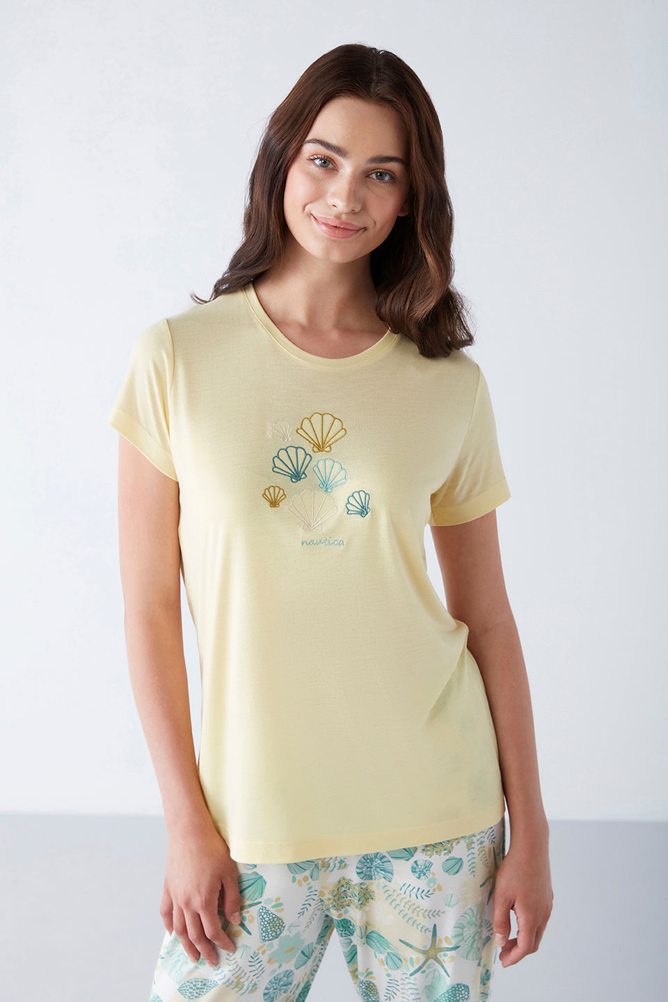 Model wearing Popjammies Women's Pyjama Set with a yellow top featuring shell designs and printed pants, smiling and posing.