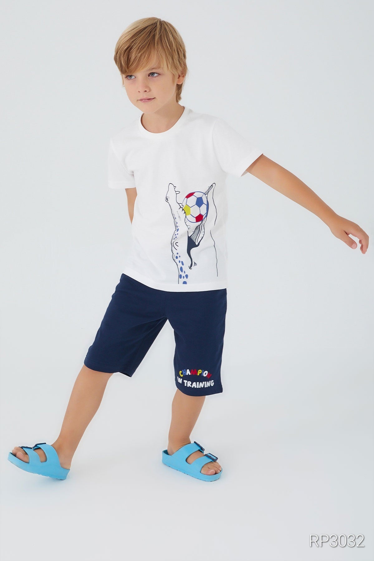 White pyjama top featuring a crocodile holding a multicolor ball design from Popjammies, paired with navy shorts waired by a blond boy