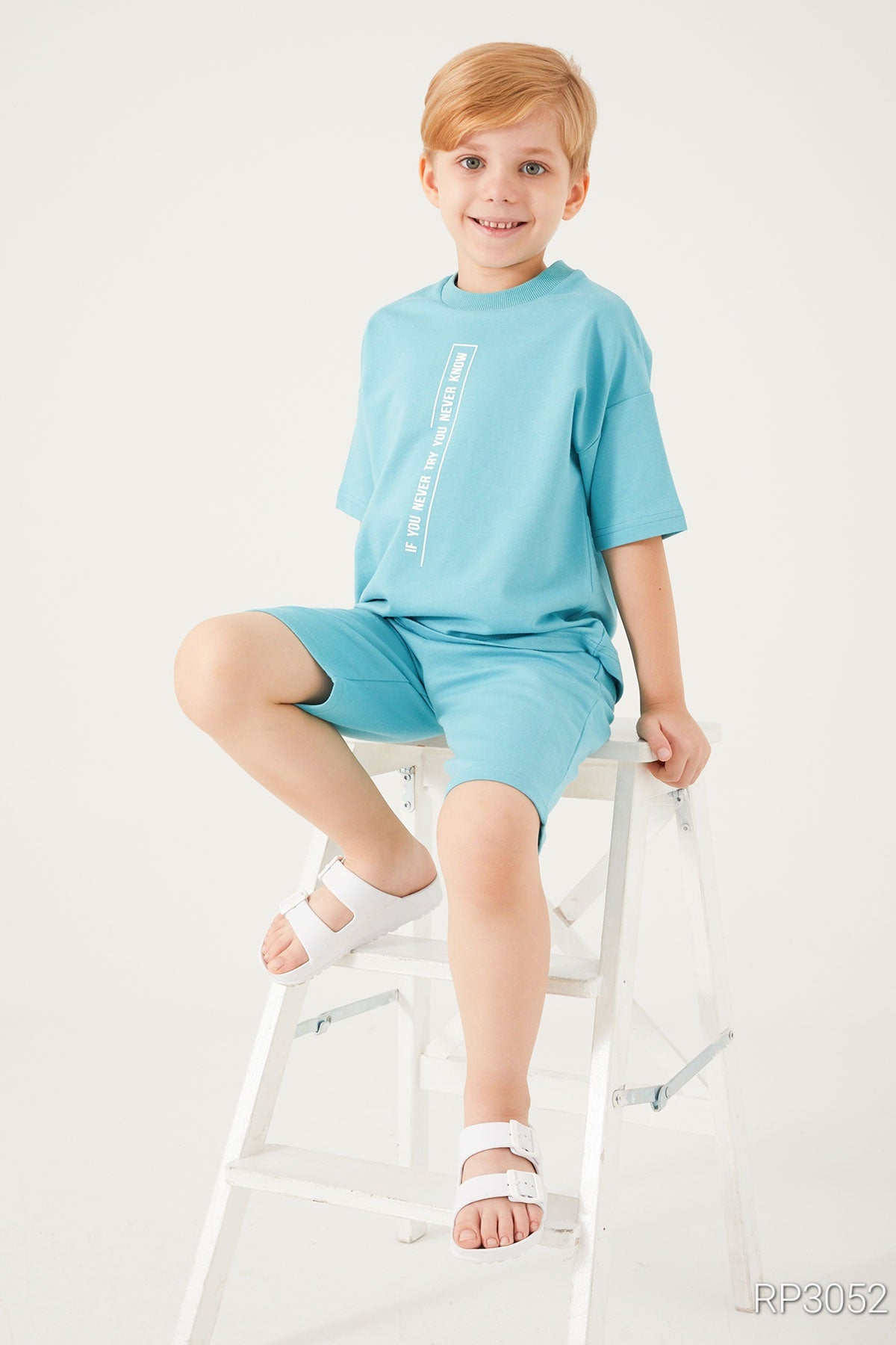 A cute boy sitting on a white chair smiling and wearing the light blue set from popjammies