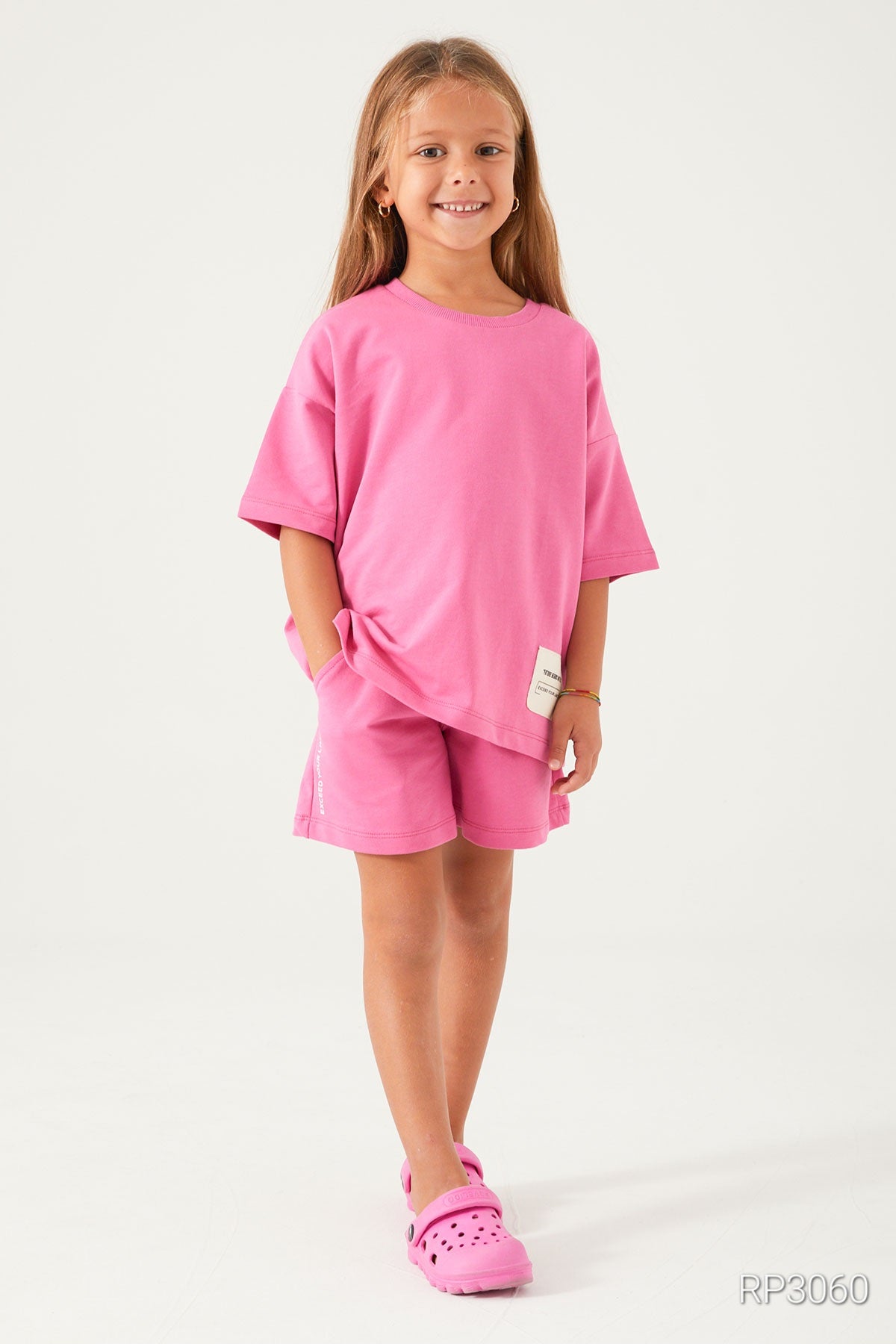 Girl wearing Popjammies Cozy Cotton Pink Matching Set with short sleeves and shorts, smiling with hand in her pocket