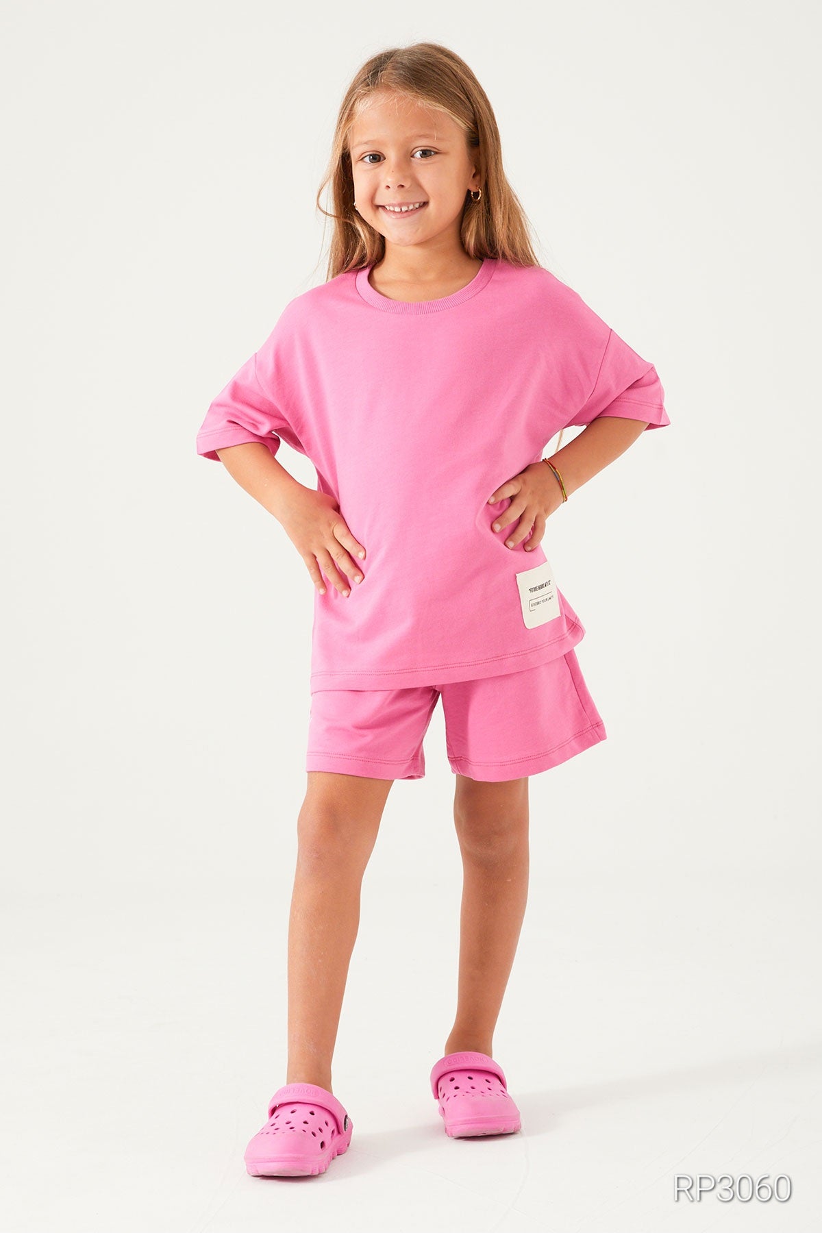 Front view of a girl wearing  Popjammies Cozy Cotton Pink Matching Set with short sleeves and shorts, showcasing the relaxed fit and playful pink design with hands on hips