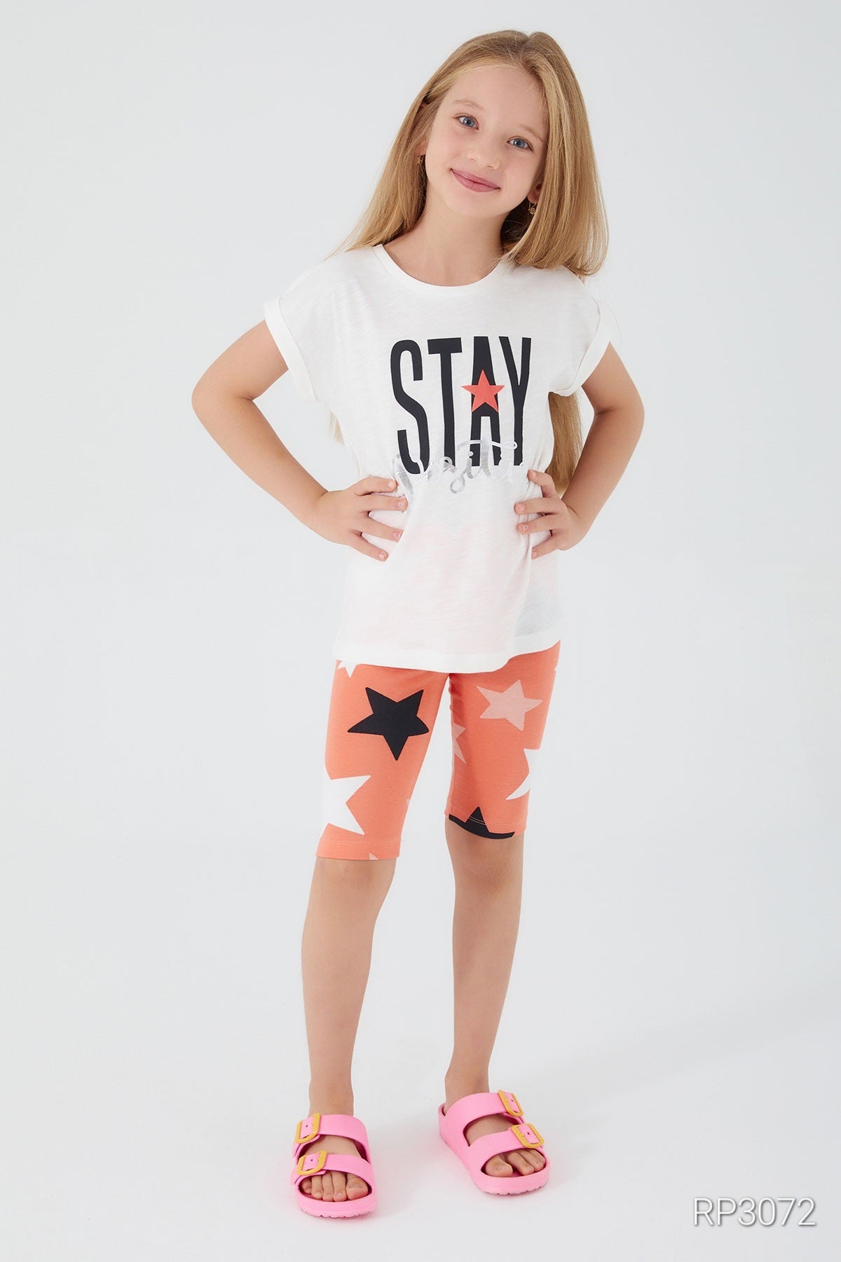 Girl wearing Popjammies 'Stay Positive' Pajama Set featuring a white top with 'Stay Positive' text and orange legging shorts with stars.