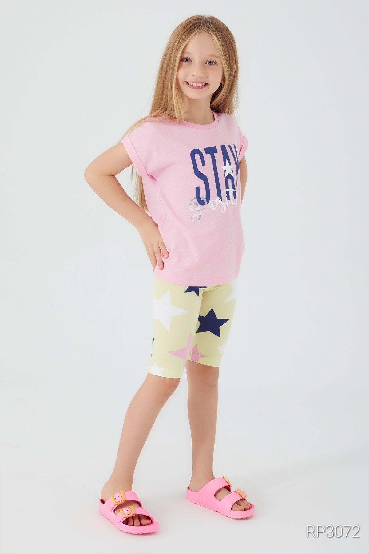 Girl wearing Popjammies 'Stay Positive' Pajama Set featuring a pink top with 'Stay Positive' text and yellow legging shorts with stars.