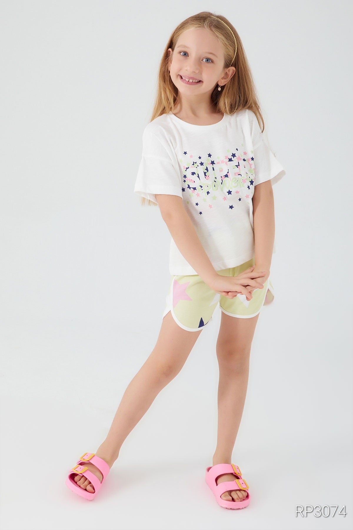 Girl wearing a white top with "Super" and colorful stars, paired with yellow shorts with stars, posing in a cute way