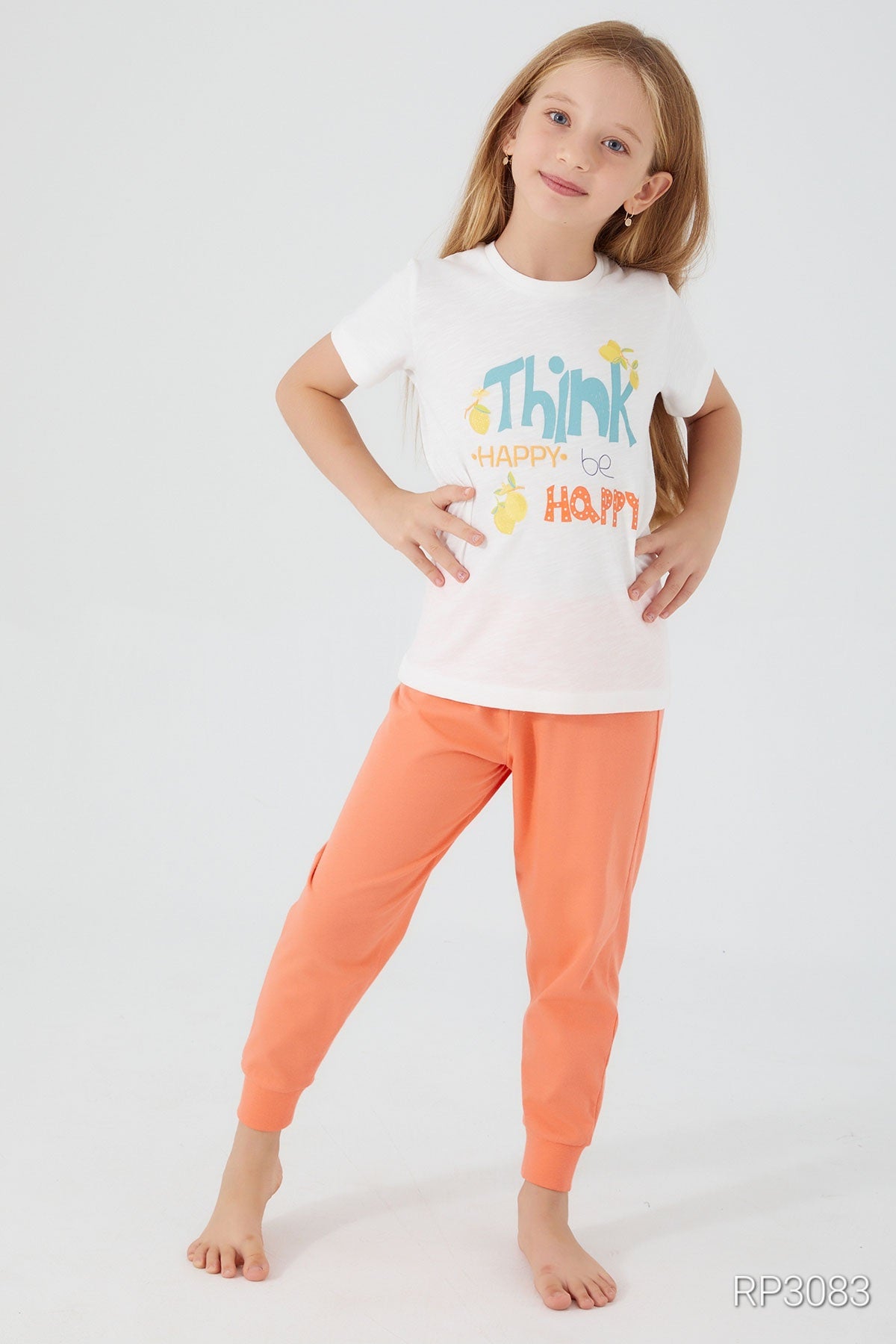 Girl wearing Popjammies Think Happy, Be Happy Pajama Set with white top and orange pants with hands on her hips