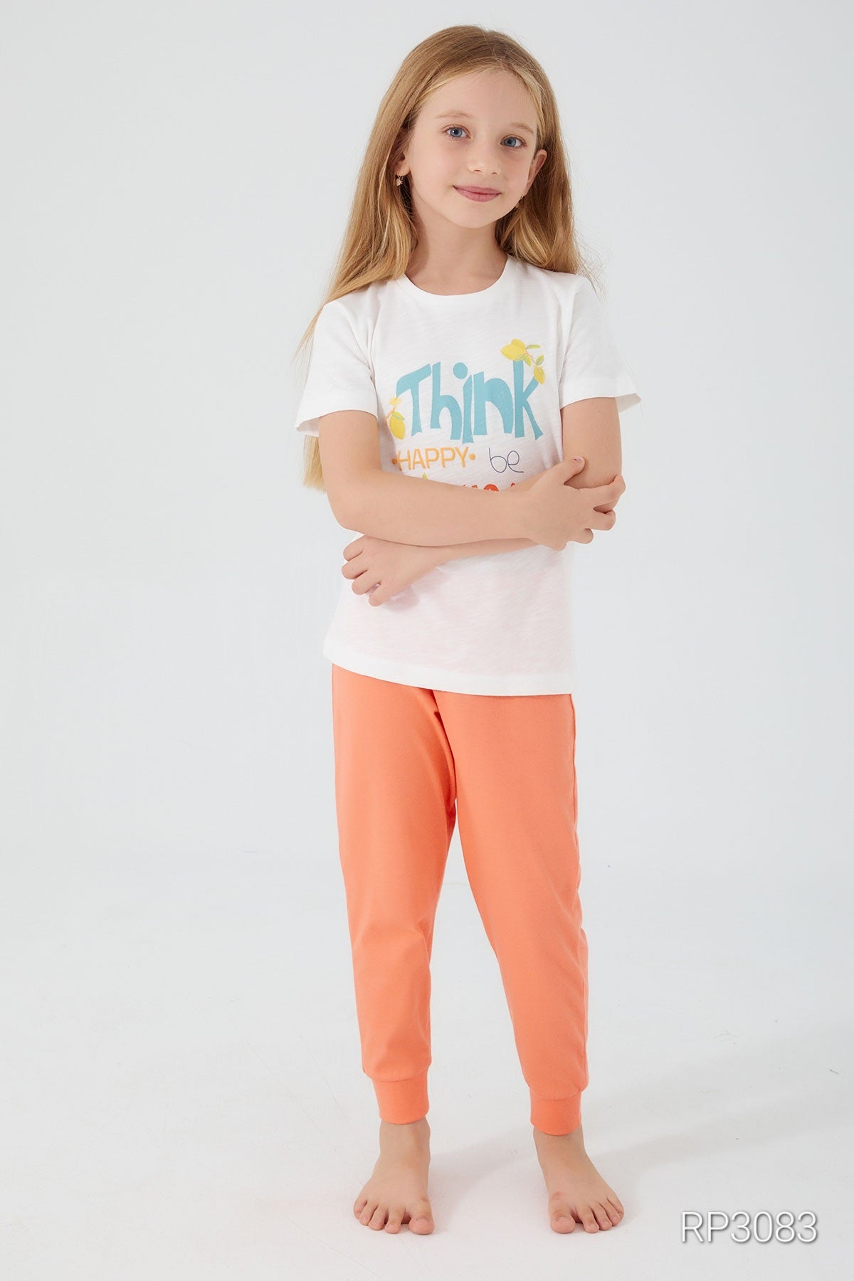 Girl wearing Popjammies Think Happy, Be Happy Pajama Set with white top and orange pants with hands closed