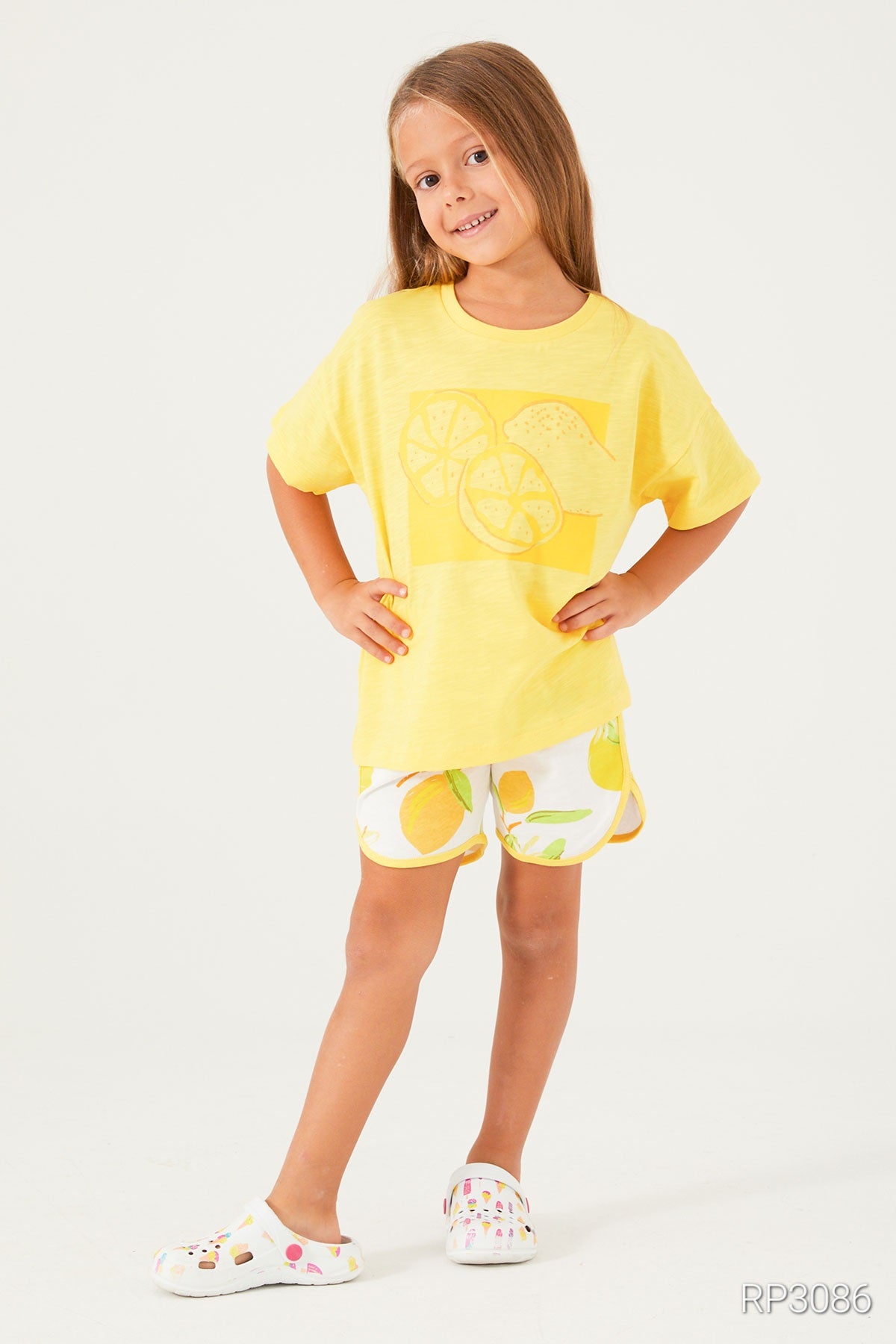 Girl wearing Popjammies Lemon Fresh Pajama Set with yellow top and white shorts with yellow lemons, posing with hands on hips