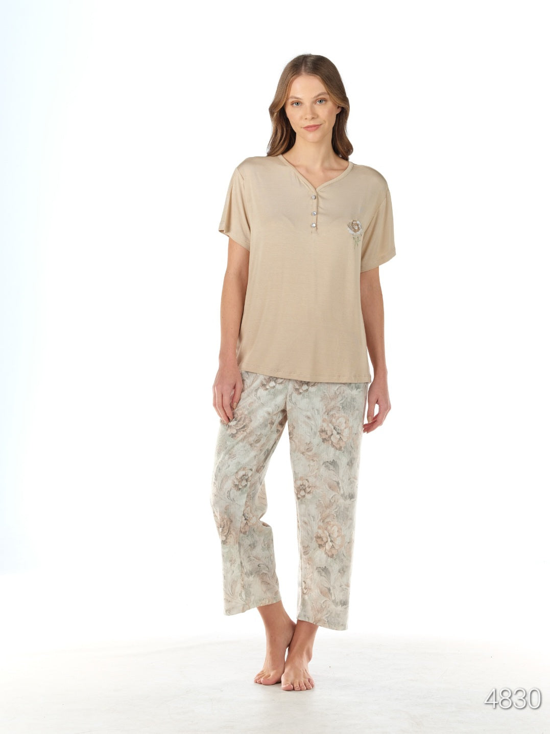 Woman wearing a beige short-sleeved top with a V-neck and capri-length floral patterned pants from the Popjammies Women's Beige Short Sleeve Top with Floral Pantacour Pyjama Set.