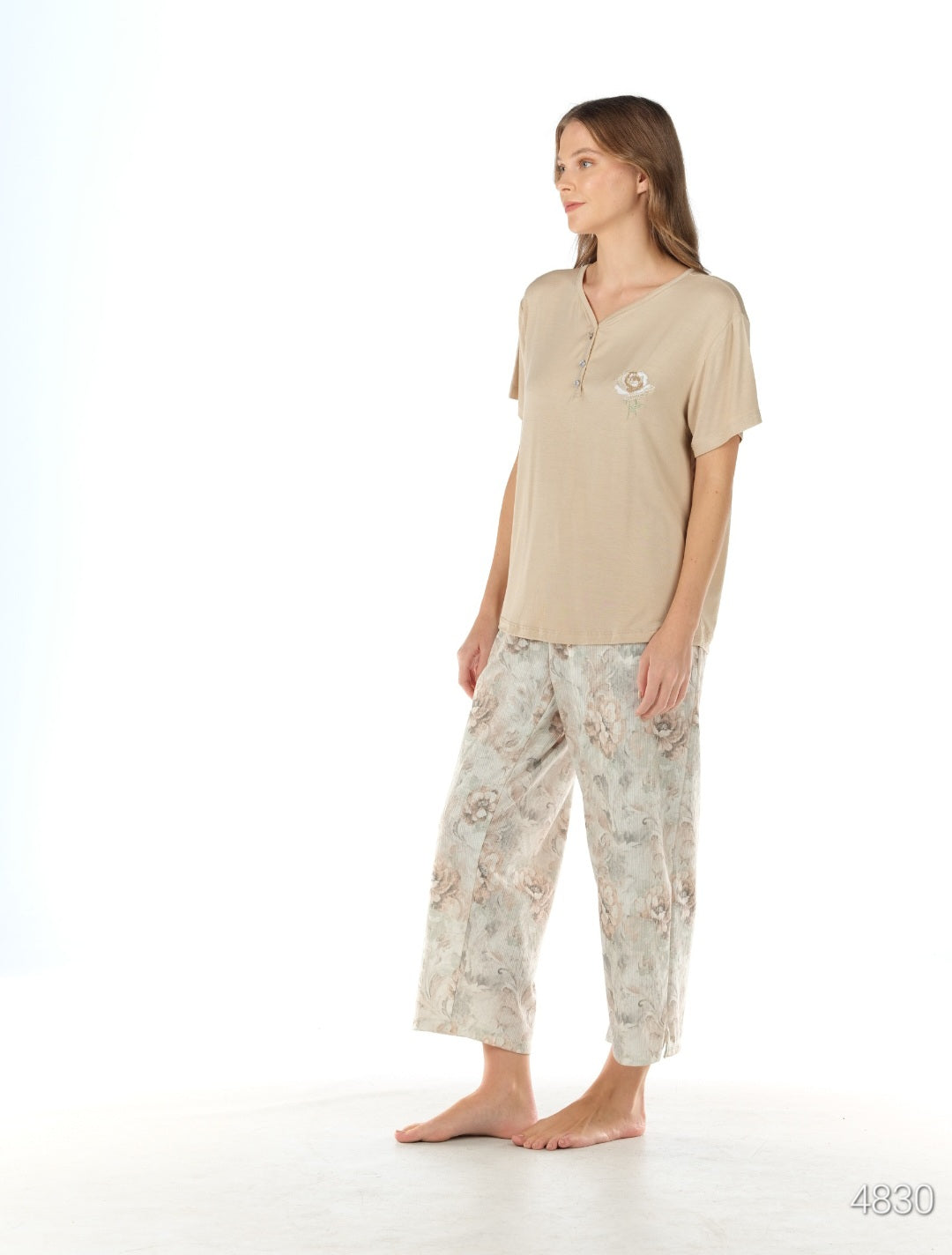 Woman standing in a beige short-sleeved top with a V-neck and floral patterned capri pants from the Popjammies Women's Beige Short Sleeve Top with Floral Pantacour Pyjama Set.