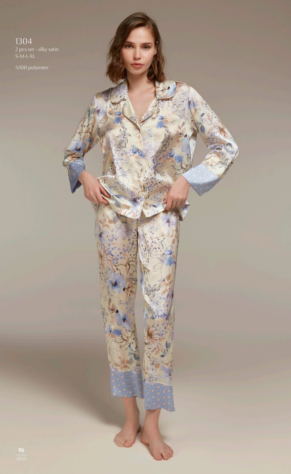 A model wearing a two-piece silky satin pyjama set from Popjammies, featuring a floral pattern in soft pastel colors, with a collared button-up top and matching pants.