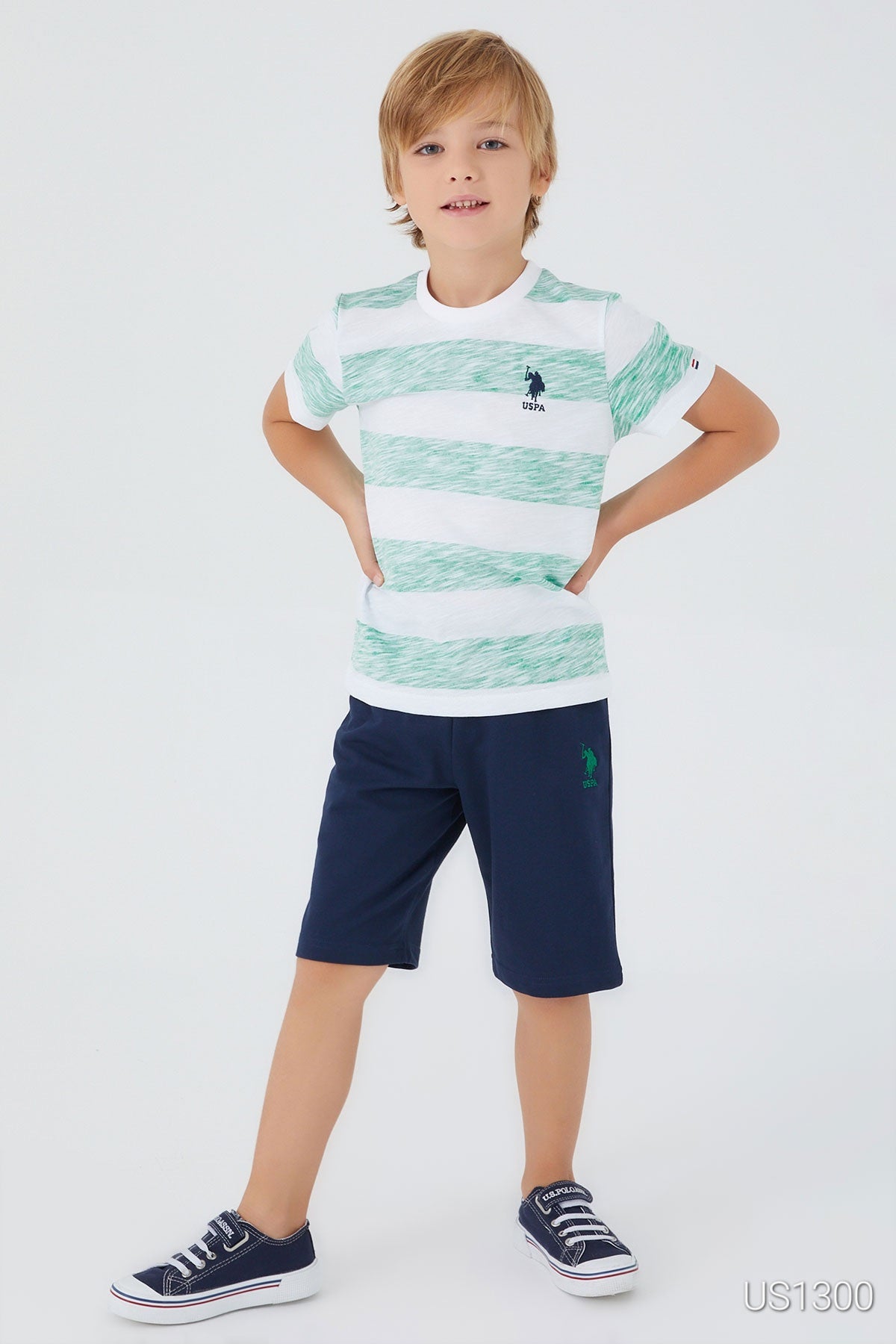 Child wearing Popjammies pyjama set with white top and large green patterns, paired with navy shorts with his hands on his hips.