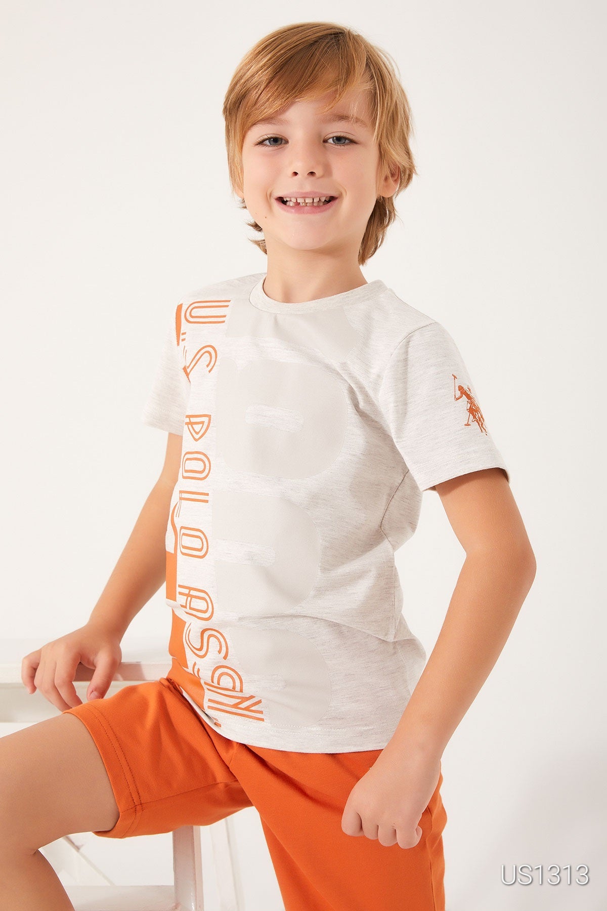 Close up of a boy wearing Popjammies pyjama set with a white tee featuring "US Polo Assn." in orange and orange shorts.