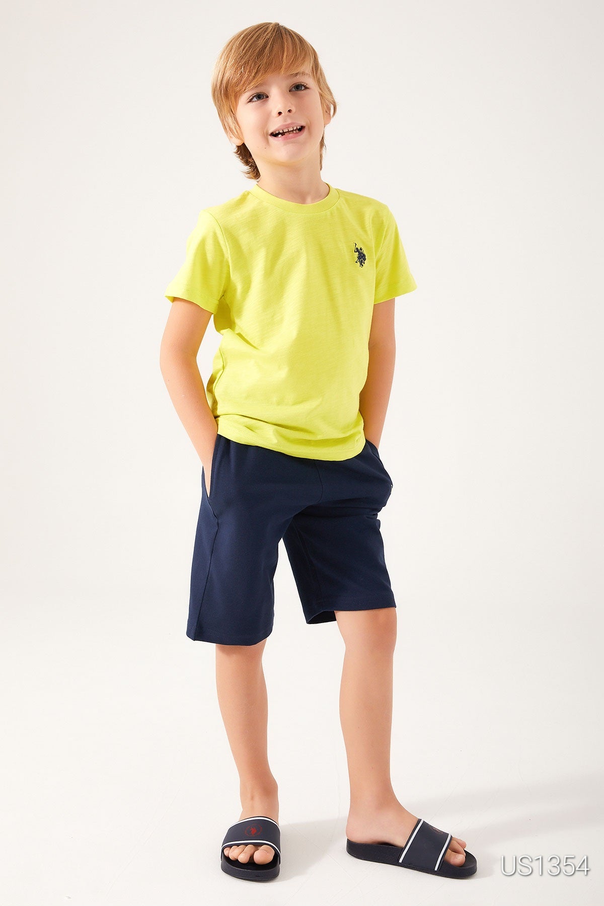 Boy wearing Popjammies Yellow USPA Top and Navy Shorts, smiling and standing with hands in pockets.