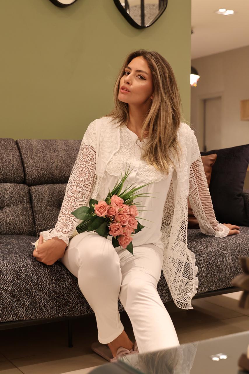 Woman in white Popjammies Floral Lace Maternity Pajama Set with lace details, sitting on a sofa and holding pink roses.