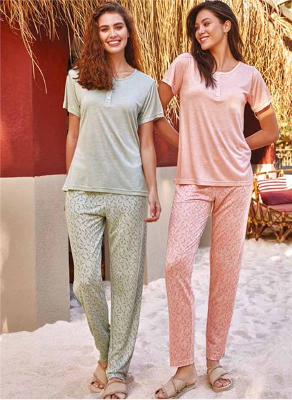 Two models wearing the Popjammies 'Dream Duo' Pyjama Set, one in mint green and the other in peach, standing and smiling in a warm, tropical outdoor setting.