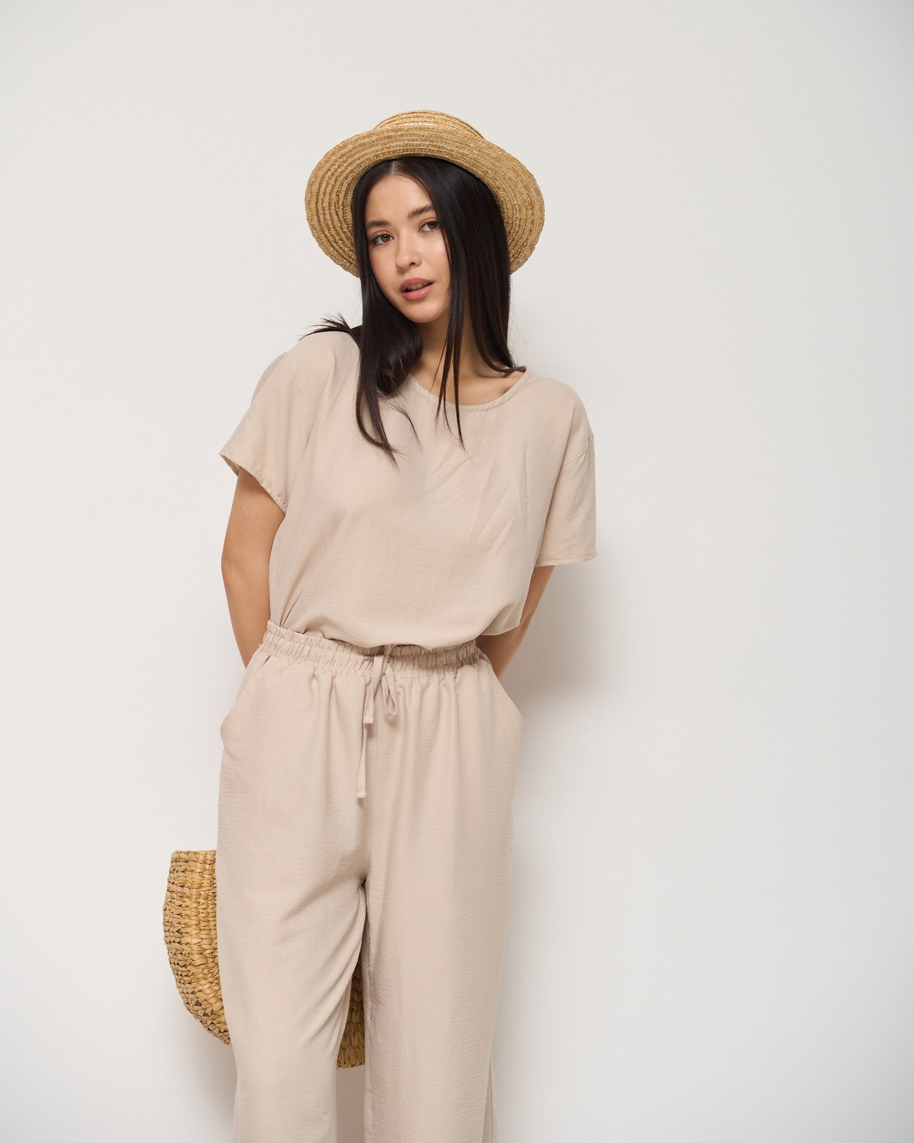 Model wearing a beige pyjama set with a drawstring waist and a straw hat, perfect for comfortable and stylish loungewear by Popjammies.