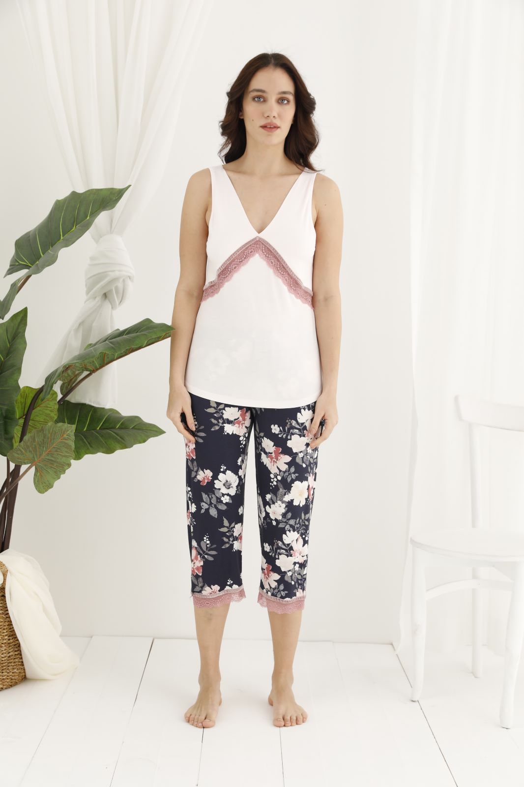 Woman wearing a white sleeveless V-neck top with pink lace trim and floral patterned navy capri pants from the Popjammies Women's Sleeveless V-Neck Top with Floral Capri Pyjama Set.