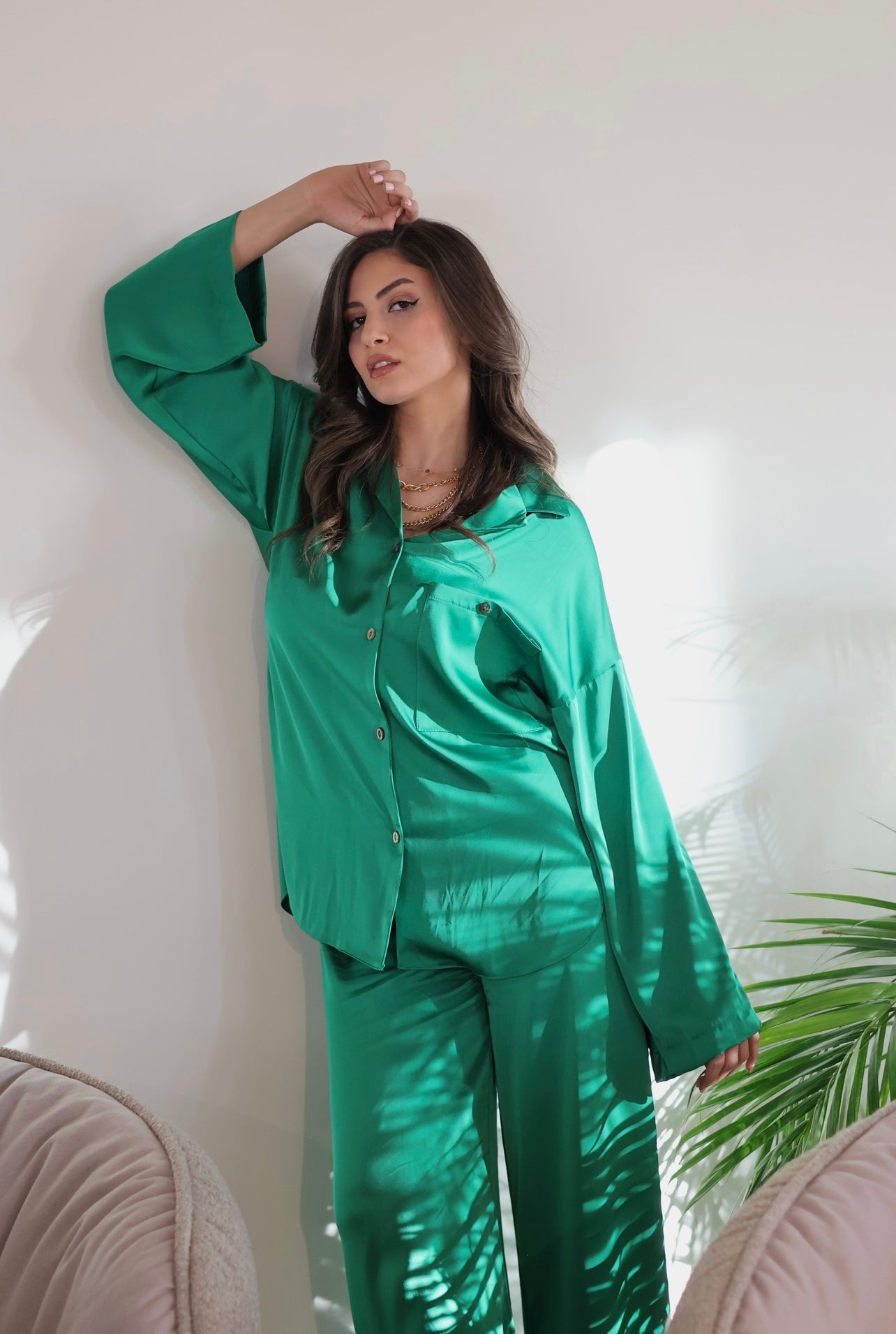 Woman wearing a green silk pyjama set by Popjammies, standing against a white wall.